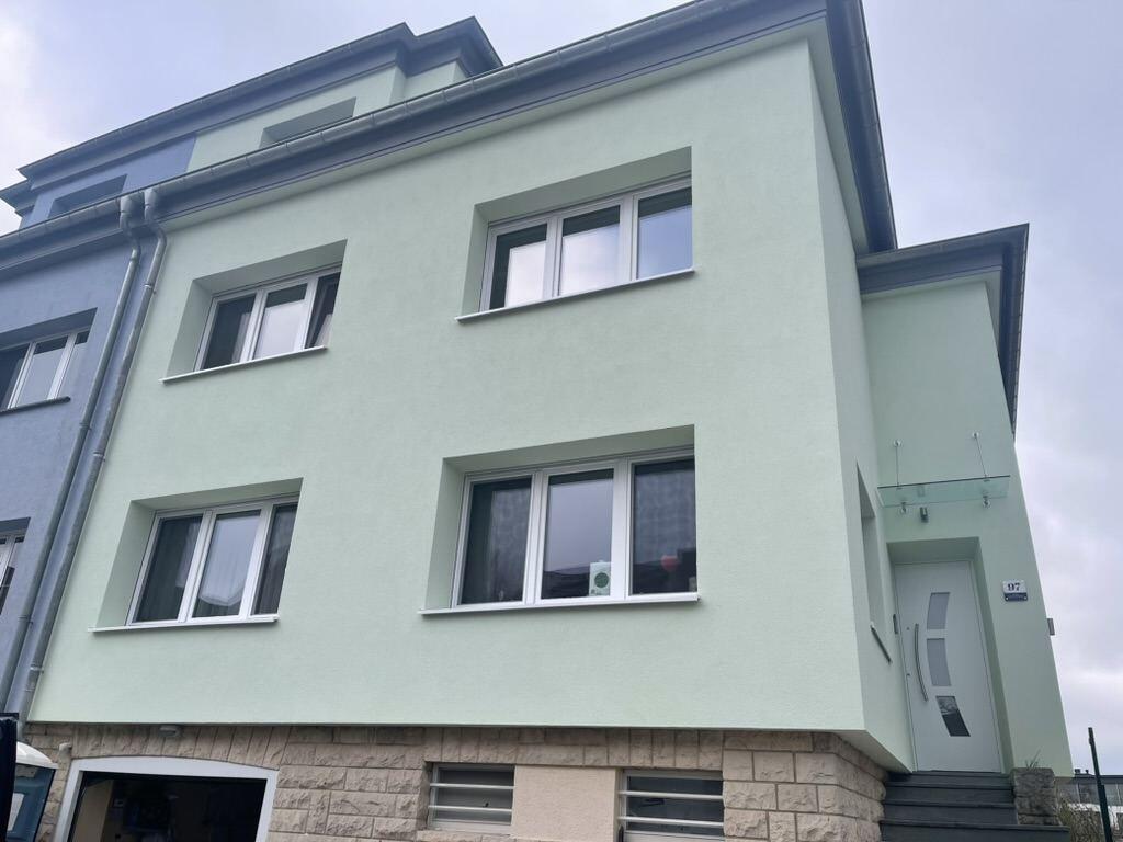 Maison après isolation par l'extérieur par BATI-LUX : nouvel enduit vert clair, fenêtres, porte et auvent en verre