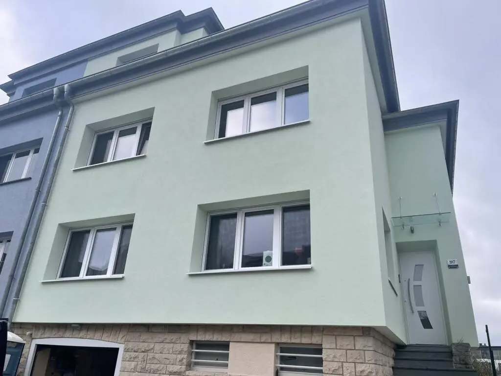 Maison après isolation par l'extérieur par BATI-LUX : nouvel enduit vert clair, fenêtres, porte et auvent en verre